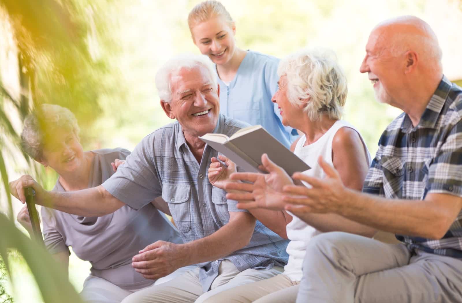 Four older adults enjoy time outdoors in their assisted living community while a caregiver checks in.
